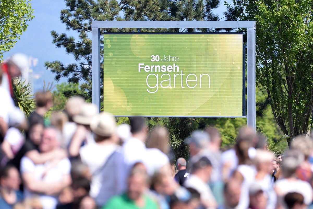 Auf dem Bild ist das Outdoor-Studio in Mainz vom ZDF-Fernsehgarten zu sehen. Verschwommen im Vordergrund ist das Publikum zu sehen. Gestochen scharf im Hintergrund ist eine Tafel in grÃ¼n zu sehen.